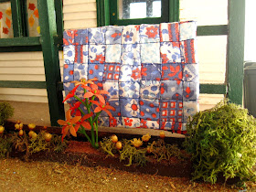 Vintage miniature quilt displayed over the front porch railing of a miniature school building.