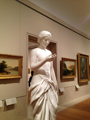 Marble statue of a man looking down at his hand in front of him holding something--could be a phone, but it's a cross