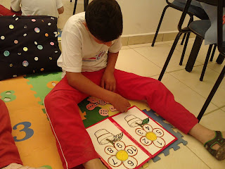 Eduardo está sentado no tapete dos números, observando as peças para relacionar número e quantidade