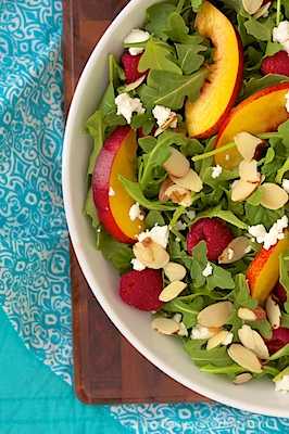 Raspberry Arugula Salad - thecafesucrefarine.com Overhead photo of a dish of Raspberry Arugula Salad on a wood cutting board and a turquoise placemat.