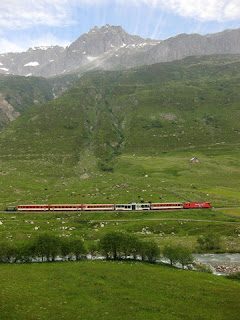 Red Swiss train crossing along the valley floor near Hospental, Switzerland