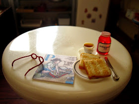 Modern miniature round kitchen table with reading glasses and magazine plus tea, toast and jam.