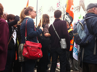 The backs of lots of people in extremely close proximity to me. Most of them are carrying flags and banners with the bottom of the flagpole about level with my eyes.