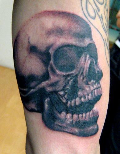 Este es un tattoo de una calavera en el brazo que tiene un agujero en el