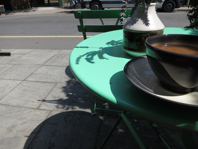 Coffee in cup on table with shadow of lavender in vase and shadow of pavement on pavement.