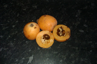 Three loquats with one cut in half so the inside of the fruit can be seen.