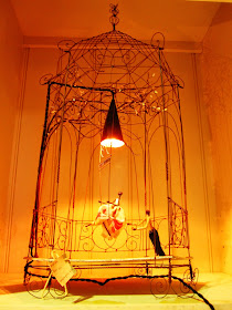 Vintage wire birdcage-shaped sculpture with wire swing and fabric dolls, used as the basis for a lamp.