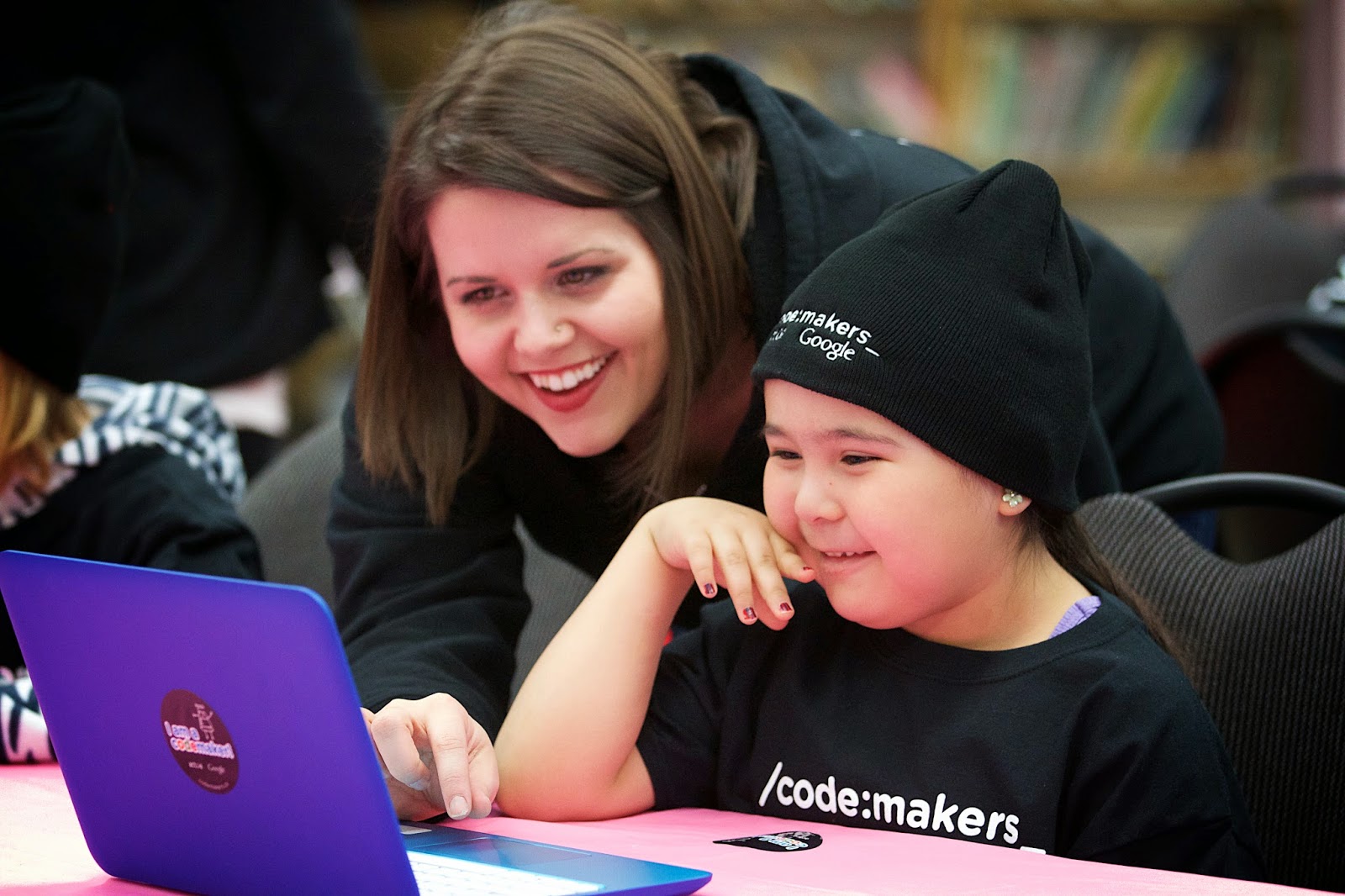 Photo of Jace Meyer of Actua working with a young student of Nakasuk Elementary helping her use coding software to remix her voice