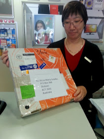 Post office assistant holding a pizza box which has been sent through the mail.