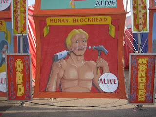 Blockhead painted sign with man drilling screws into his face