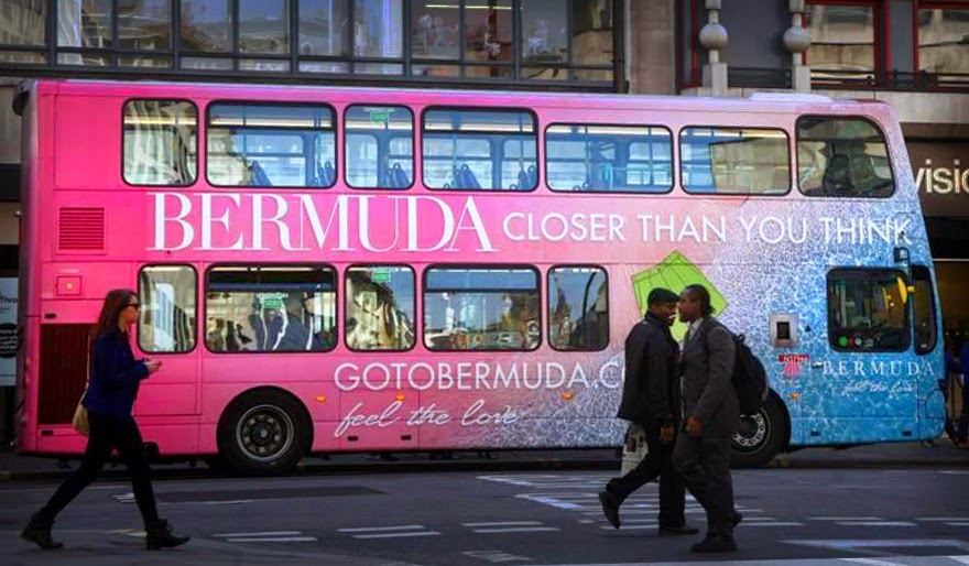 Bright pink and turquoise double decker bus advertising Bermuda