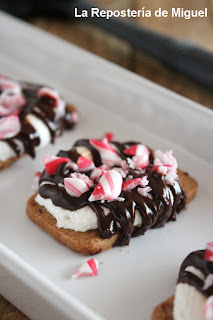Fotografía de la receta anteror de una porción de galleta cubierta con una nube de azúcar e hilillos de chocolate negro y trozos de bastón de caramelo.