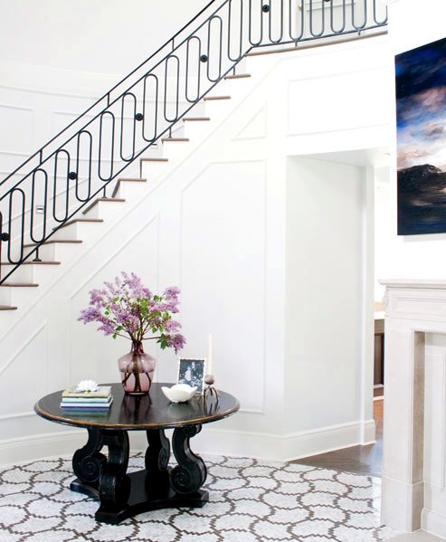 Foyer with grand staircase, a round dark wood table and marble mosaic tiles