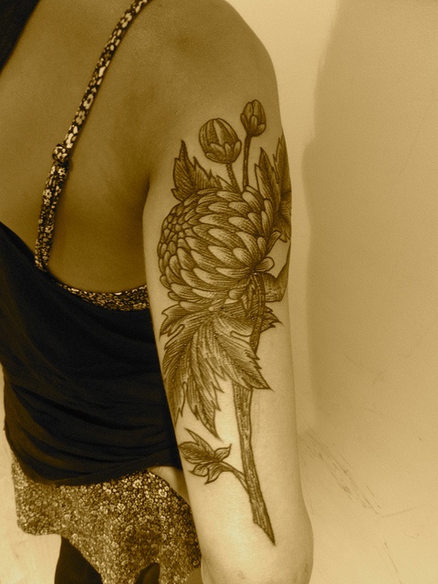 Czarno szary tatuaż kwiatu z łodygą na ramieniu