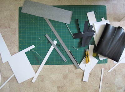 Large cutting board, ruler, stanley knife and various bits of card and paper on a kitchen floor.