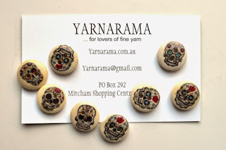Wooden buttons with decorated skulls painted on them, packaged with Yarnarama's business card.