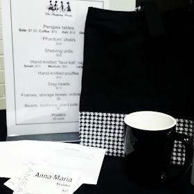Black and white bag and mug on a sales table at a conference, with a conference badge in the front.