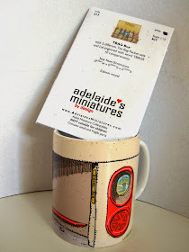 Trevor Dickinson Canberra bus shelter mug with miniature tea bag box kit sticking out of it.