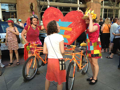 Two women with two bikes attached with state of Minnesota shape between and a heart and equal sign on it