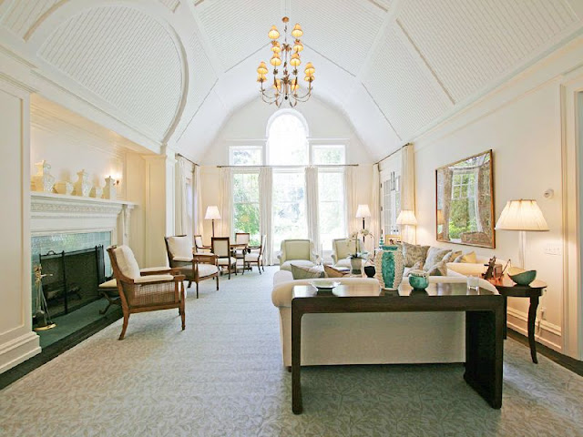 alternative view of the livng room with high, white, gambrell ceilings, a fireplace with traditional decor and a large chandelier