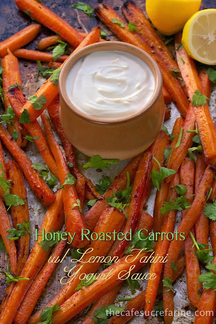 Honey Roasted Carrots - thecafesucrefarine.com A vertical photo of a baking pan filled with Honey Roasted Carrots with a small jar of lemon tahini yogurt sauce in the middle and a graphic title at the bottom of the photo.