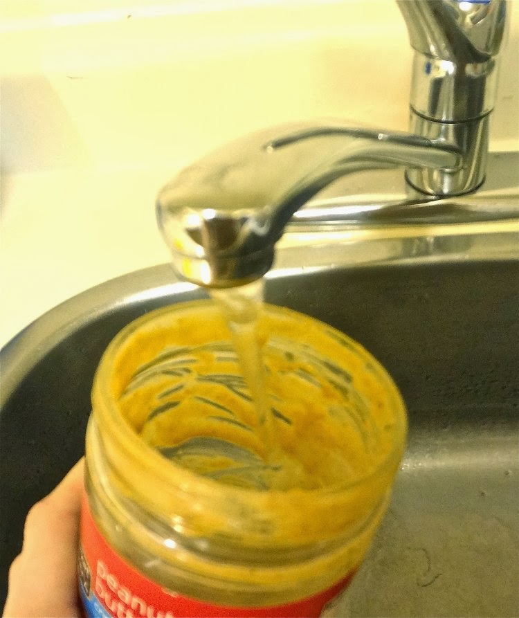 Cleaning a dirty peanut butter jar with soapy water.