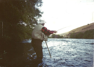 A picture of Don Wilson standing in the Deschutes River landing a steelhead with his fly rod.