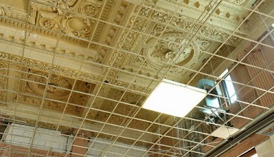 Ornate coffered ceiling with metal grid for ceiling tiles and box fluorescent lights in some of the grid spots