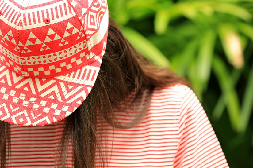 Maria Copello fashion blogger at notesofstyle is wearing an oversized striped top with denim shorts, gold oxfords and printed hat.