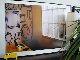 A1-sized photo of a dolls' house miniature scene in a frame with a 1/12-scale table in front of it..