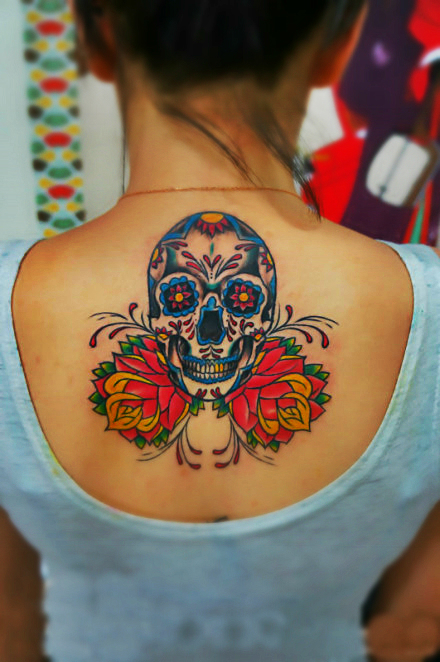 A colorful sweet sugar skull tattoo on the back with flowers