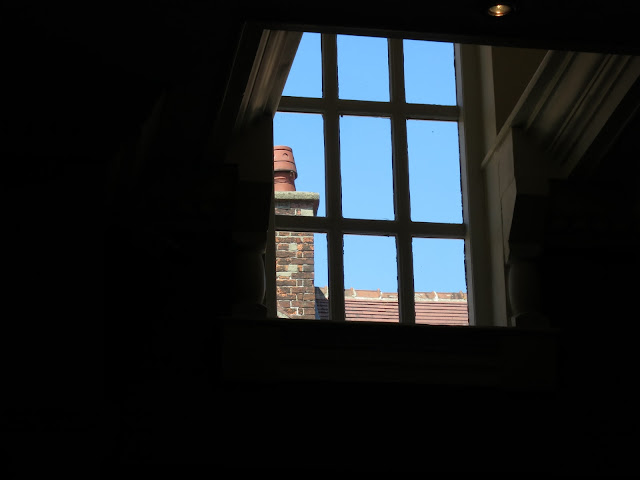 Looking through window with nine panes at chimney and red tiled roof beyond.
