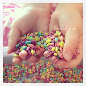 Child's hands holding rainbow-coloured barley grains for sensory play