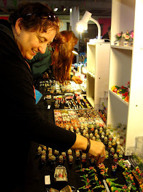 Woman browsing the goods for sale at a market stall selling dolls' house miniatures.