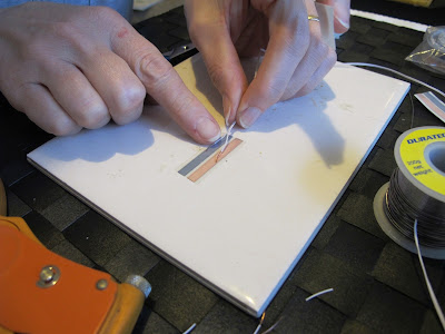 Woman placing wires onto a run of copper tape to a tile.