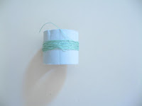 Side view of cardboard reel with a remnant of green size 80 cotton thread.