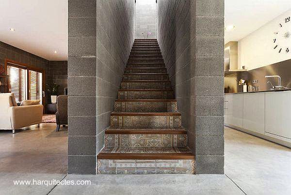 En el centro de la planta baja dos muros sirven de caja para la escalera cubierta de cerámica decorativa gris Escalera de concreto en el centro del nivel inferior