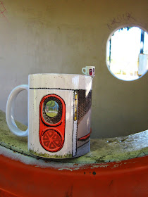 Dolls' house miniature mug with a Canberra bus shelter print, balanced on the edge of a full-sized Canberra bus shelter mug, sitting on the window ledge of a Canberra bus shelter.