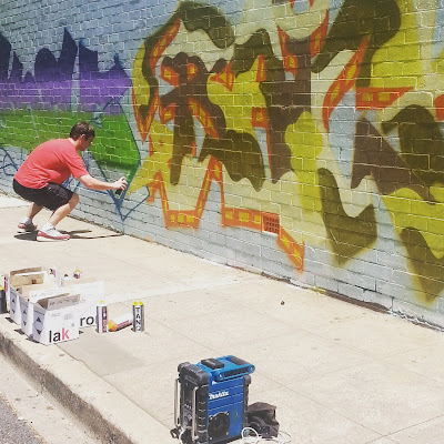 Man spray painting street art on a wall.