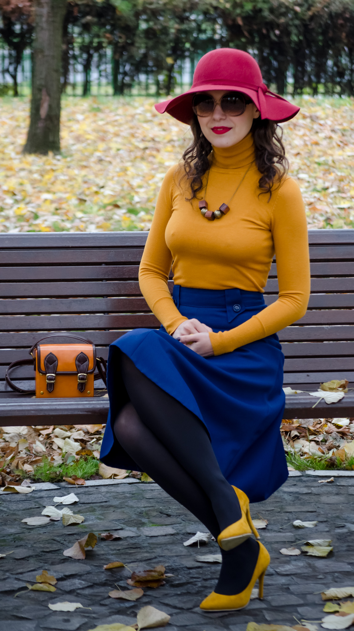 blue skirt mustard turtleneck sweater burgundy floppy hat brown jacket box satchel mustard heels autumn fall scenery leaves