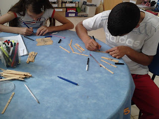 Filipe a Amanda preparando o jogo dos palitinhos, com palitos de picolé e canetinha.