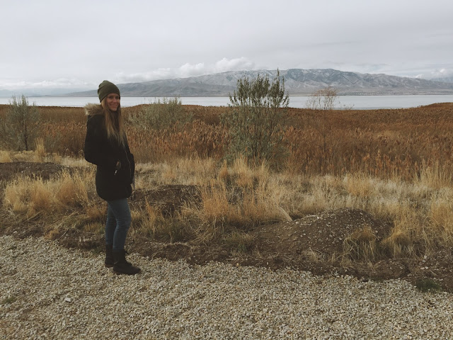 A blonde girl stands bundled up and smiling by a lake in the early winter. // THE JOY BLOG
