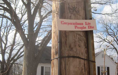 Handmade sign nailed to a utility pole, reading Corporations lie, people die