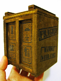 A hand holding up a miniature wooden packing crate.