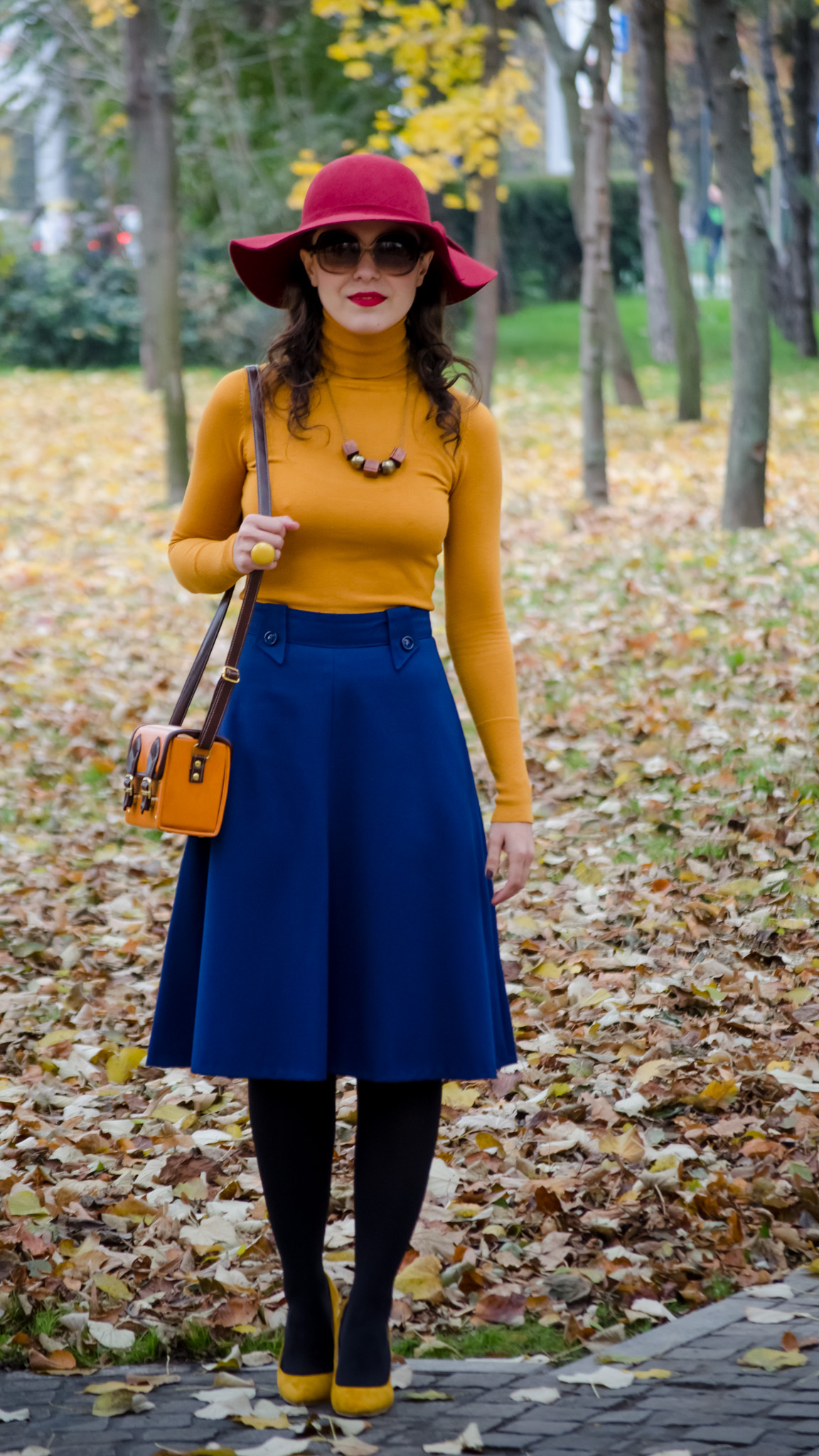 blue skirt mustard turtleneck sweater burgundy floppy hat brown jacket box satchel mustard heels autumn fall scenery leaves