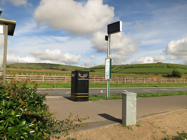 Bus stop, shelter and empty digital sign with open country and sky in background.