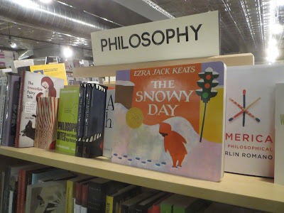 Picture book The Snowy Day sitting on a shelf of books labeled Philosophy