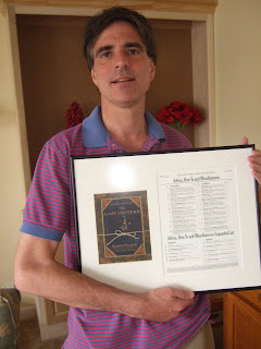 Randy Pausche in an incredibly scary blue and pink striped shirt, holding a framed picture of the cover of his book.