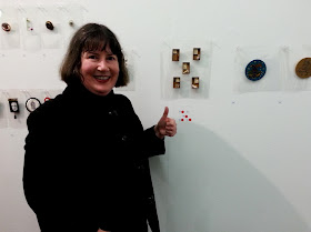 Woman looking happy and making a thumbs up sign in front of five brooches with four red dots.