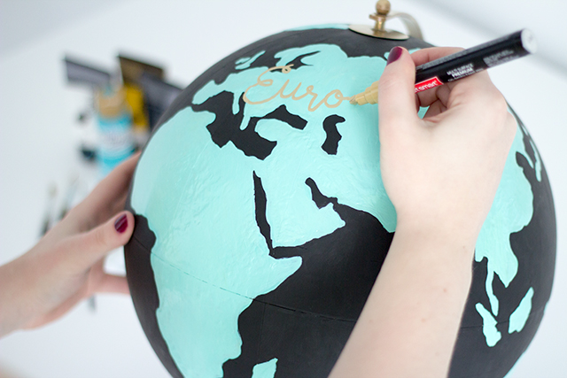 DIY Anthropologie inspired wanderlust globe. Use a gold paint pen to write continent names on your DIY Anthropologie inspired wanderlust globe.